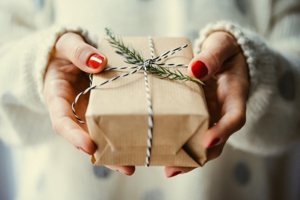 Zwei H&auml;nde halten ein in Packpapier gewickeltes Geschenk mit Zweig
